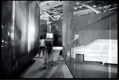 半透明のガラスパネルが迷宮状に並ぶ『Les immatériaux』展の会場写真（白黒）。来場者がパネルの間を歩いている。