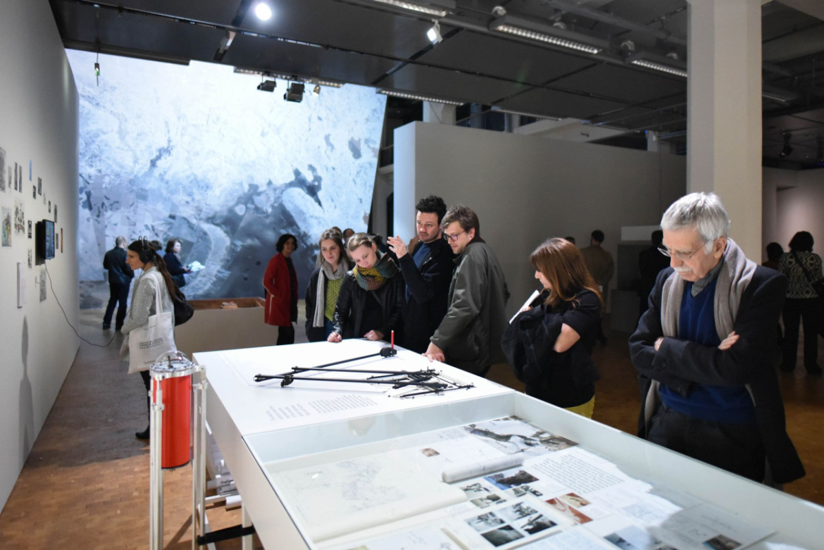 ZKM『Reset Modernity!（リセット・モダニティ！）』展の会場風景。文書や写真などの資料が広げられた大型テーブルを複数の来場者が囲み、資料を眺めている。